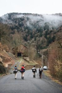 Group of backpackers walking on a misty mountain road surrounded by lush foliage.