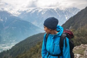 Woman hiking in mountain landscape with snow-capped peaks and a cloudy sky.